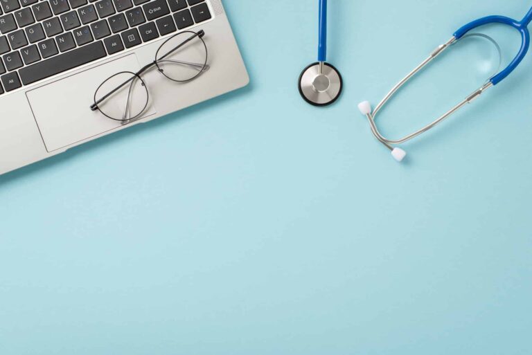 A laptop, eyeglasses, and stethoscope placed on a blue background, symbolizing a family-owned clinic with a focus on personalized healthcare services.